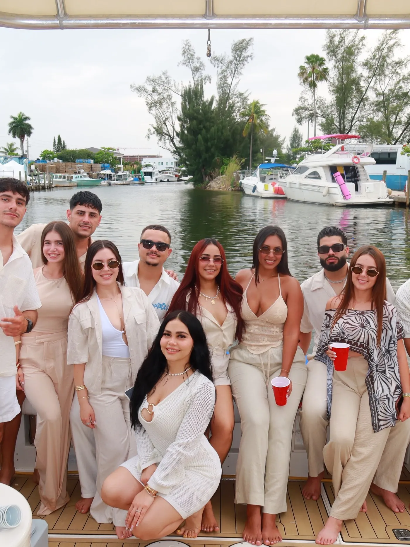 A group of twelve guests in coordinated cream outfits on the aft deck, a marina behind them
