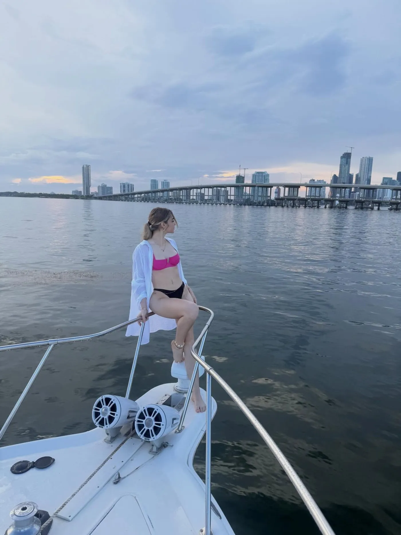 A guest sitting on the bow rail, the Miami skyline and causeway across the water