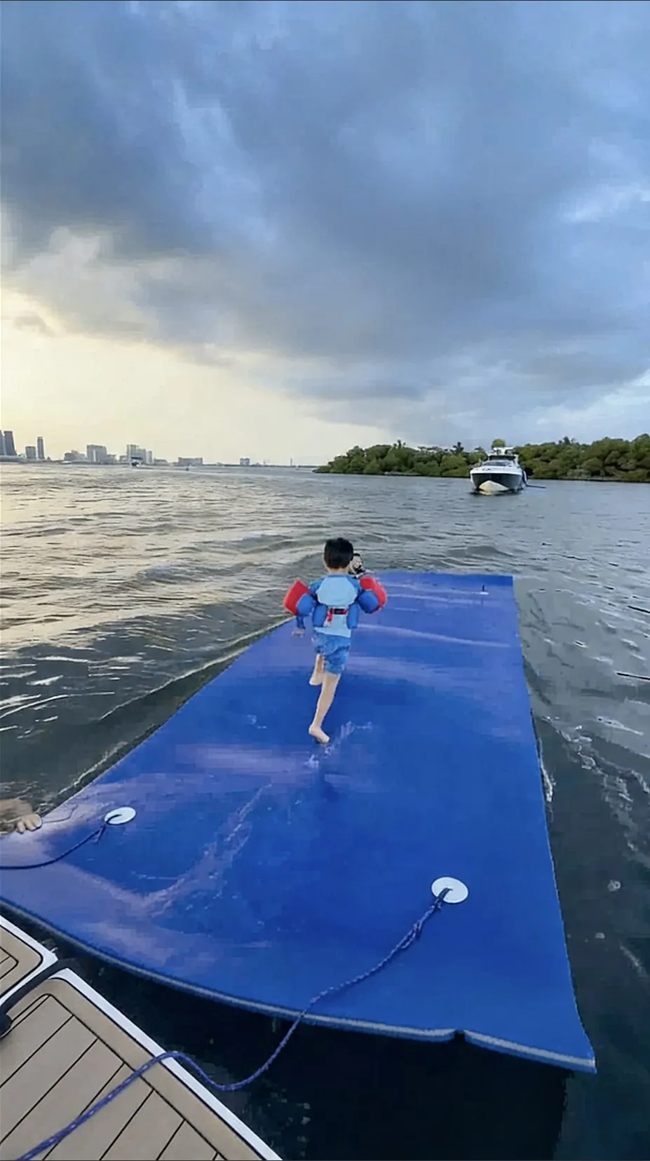 A child running along a floating water mat trailed behind the boat, storm cloud over the skyline