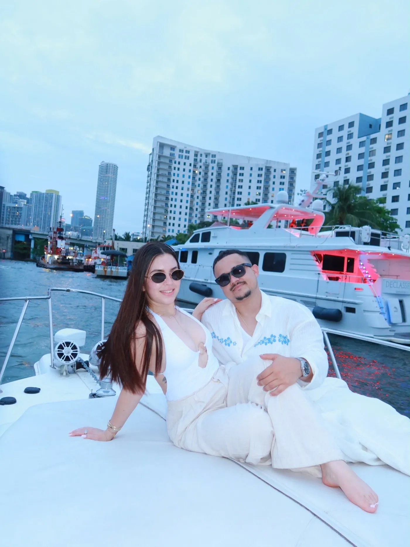 A couple sitting together on the bow, Miami apartment towers and moored yachts behind