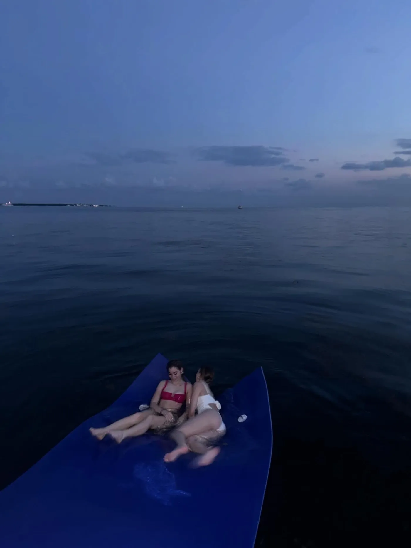 Two guests resting on the floating water mat at dusk on a calm bay